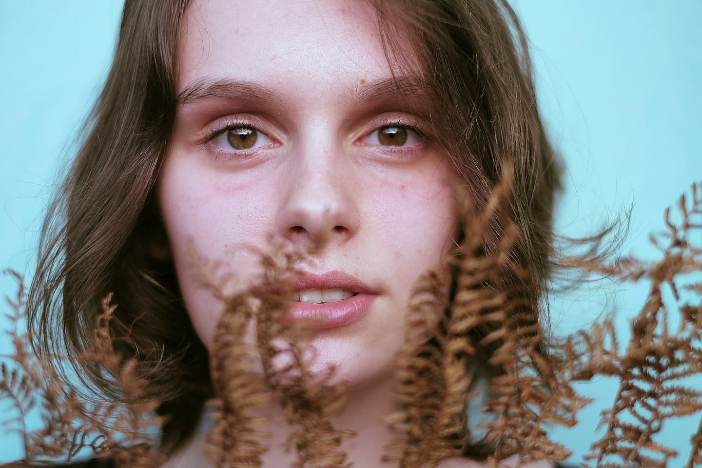 Donna con capelli castani che guarda tra foglie di felce secca.