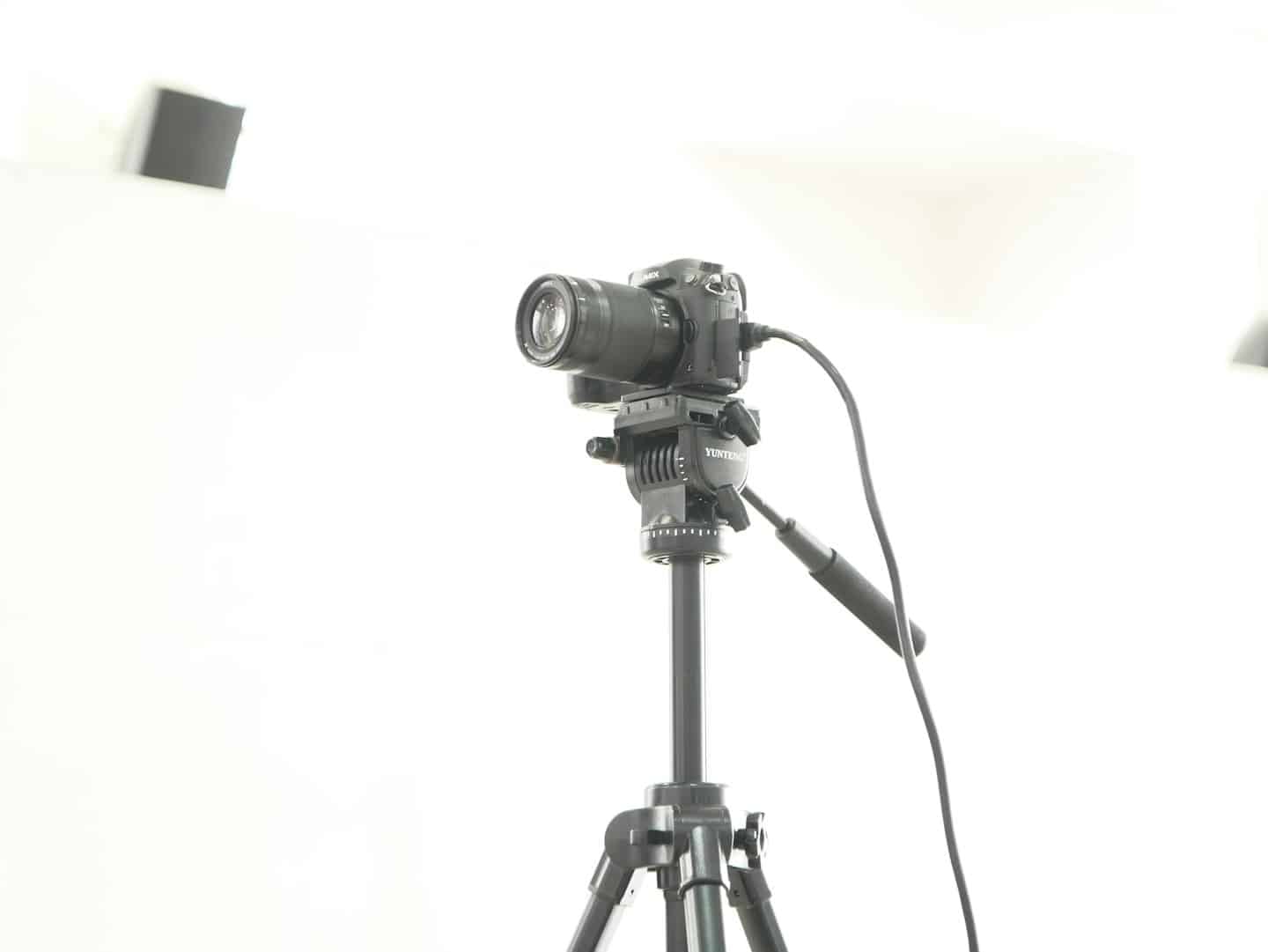 Macchina fotografica professionale su treppiede con cavo su sfondo bianco.